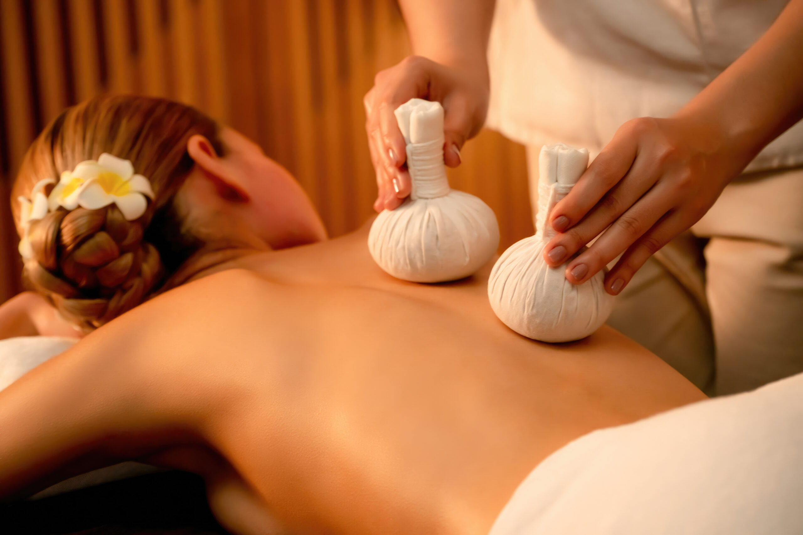 Hot herbal ball spa massage body treatment, masseur gently compresses herb bag on woman body. Tranquil and serenity of aromatherapy recreation in warm lighting of candles at spa salon. Quiescent