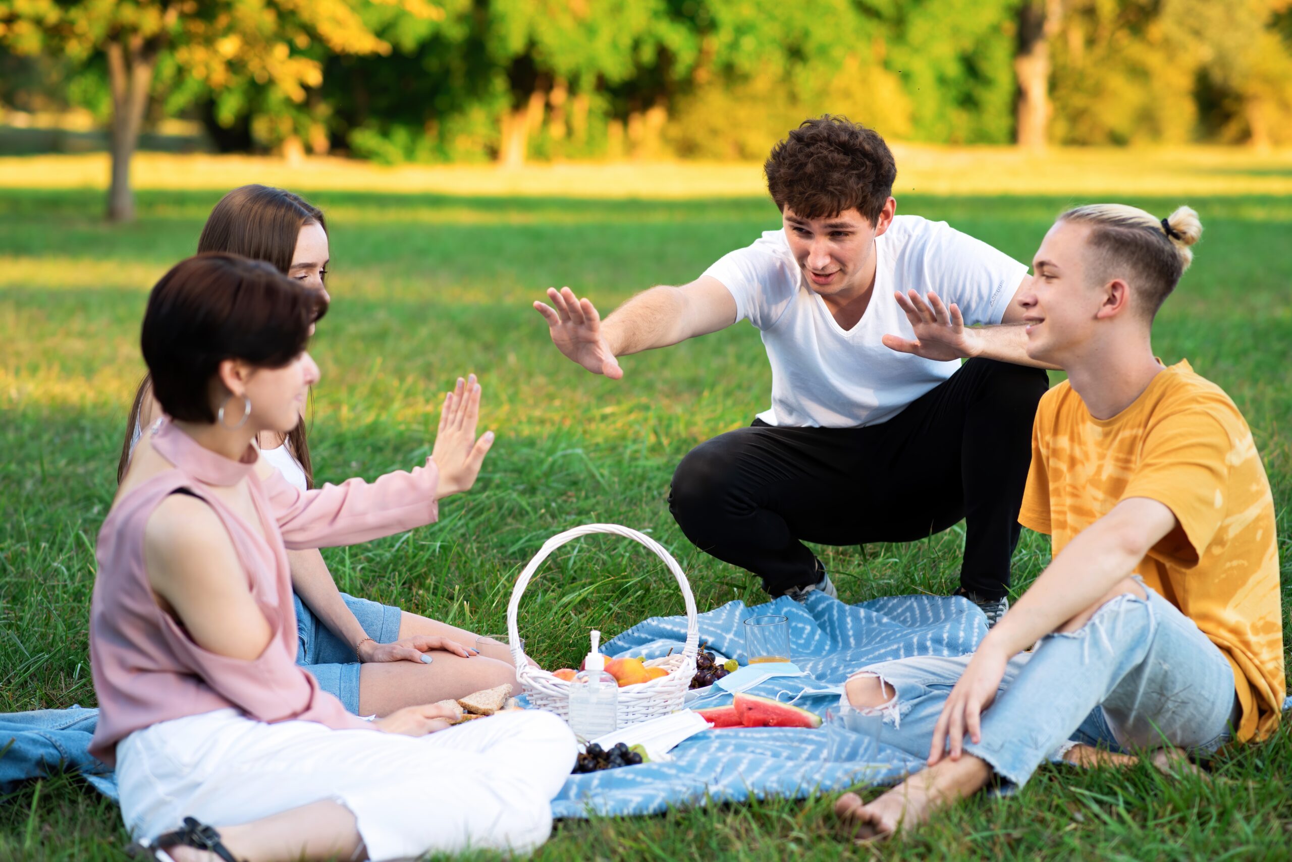 Group of friends having fun at a picnic blanket with goodies, in a park during the pandemic in Chisinau, Moldova