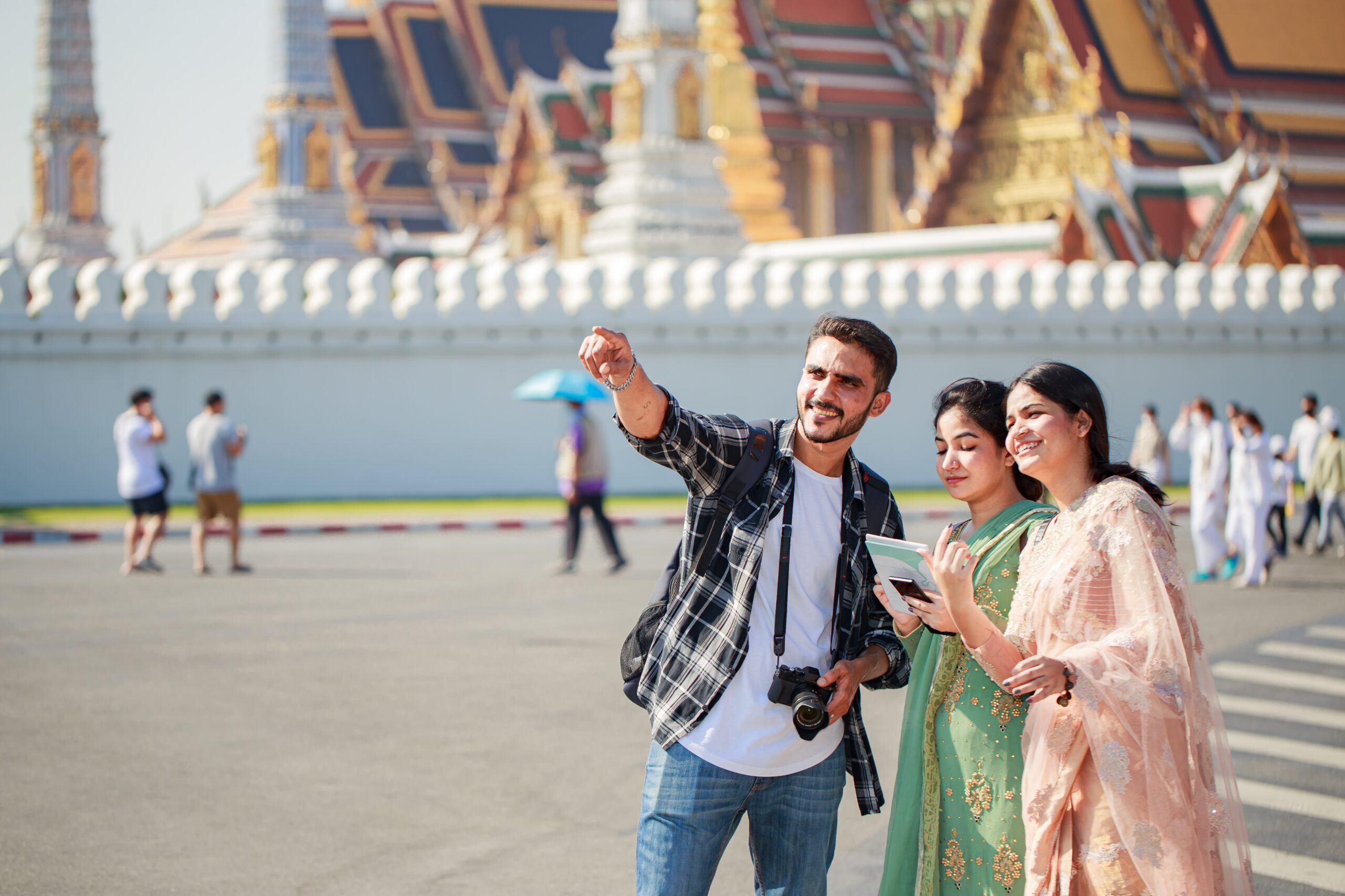 South Asian tourists backpackers looking a map for direction while traveling around traveling on holidays tourist landmark behind Wat Phra Kaew or Emerald Buddha Temple Bangkok Thailand.