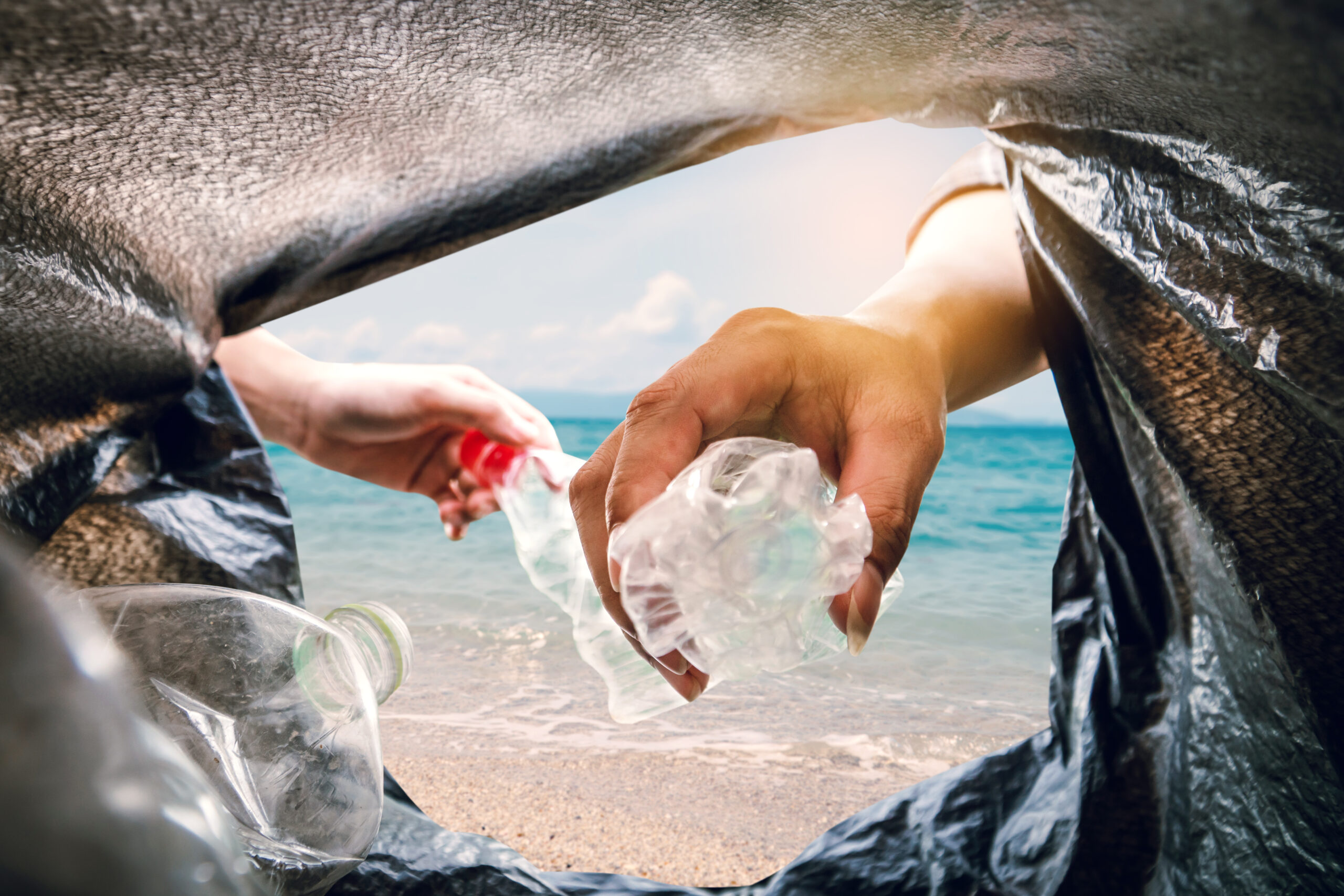 The volunteer picking up a bottle plastic in to a bin bag and the sea background ,recycling and protect environment from a pollution concept.
